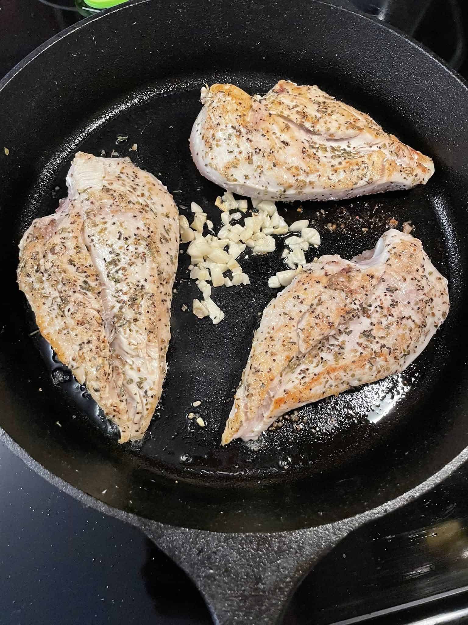 Seared chicken breasts in skillet with freshly chopped garlic starting to cook