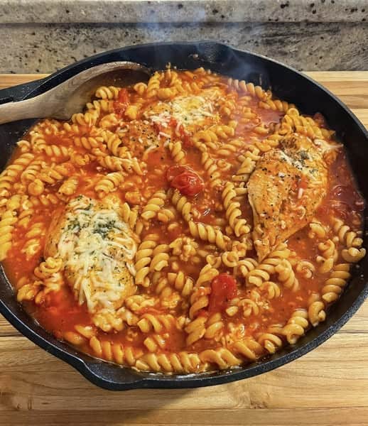 Overhead shot of cast iron skillet filled with baked chicken pasta and fusilli in tomato sauce