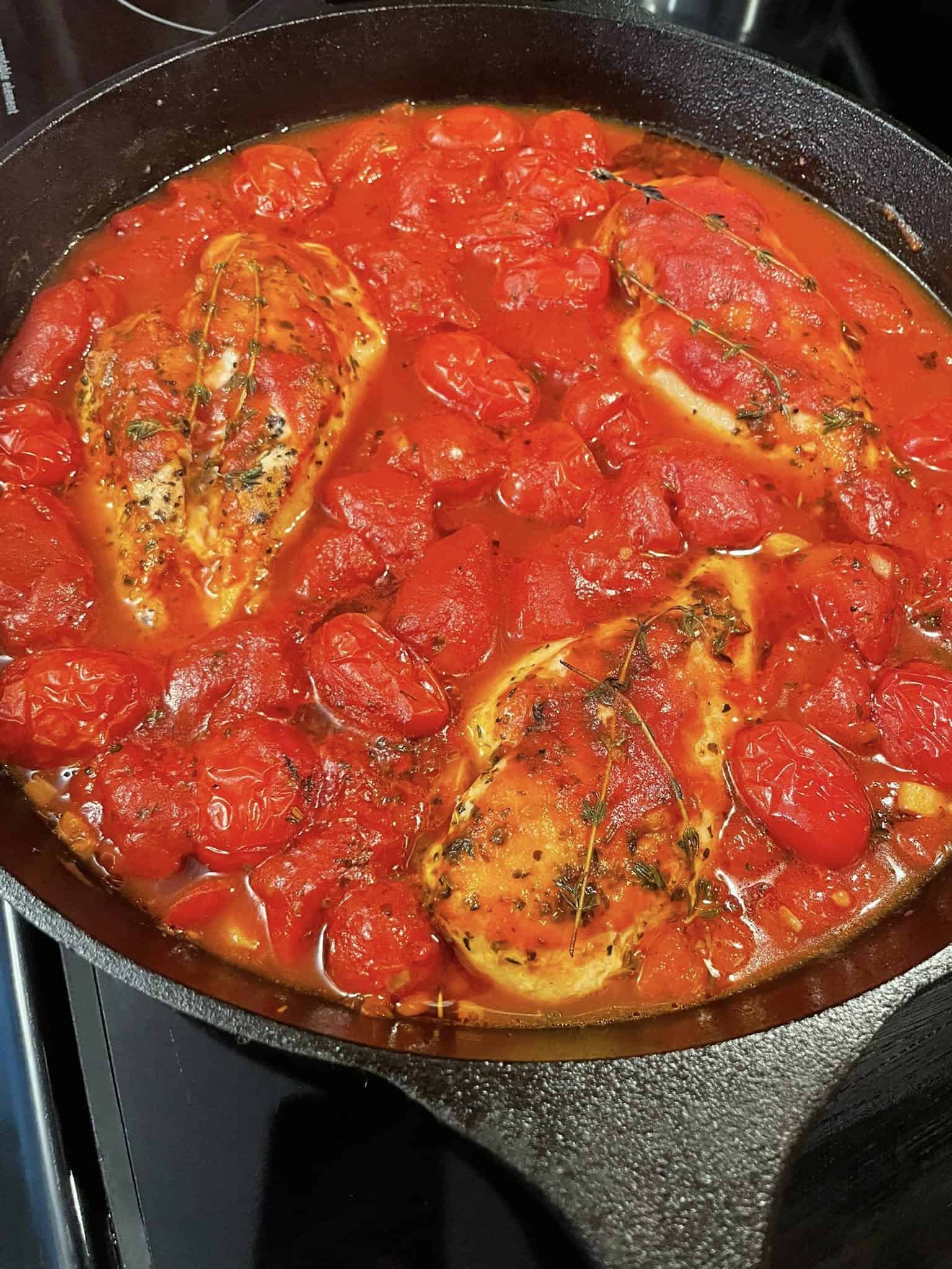 Chicken breasts simmering in a rich tomato sauce with whole cherry tomatoes and thyme sprigs