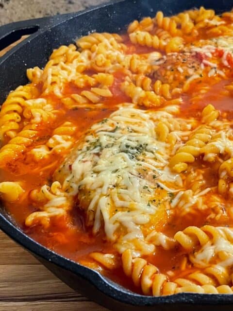 Fusilli pasta and Parmesan cheese added to the skillet with tomato chicken