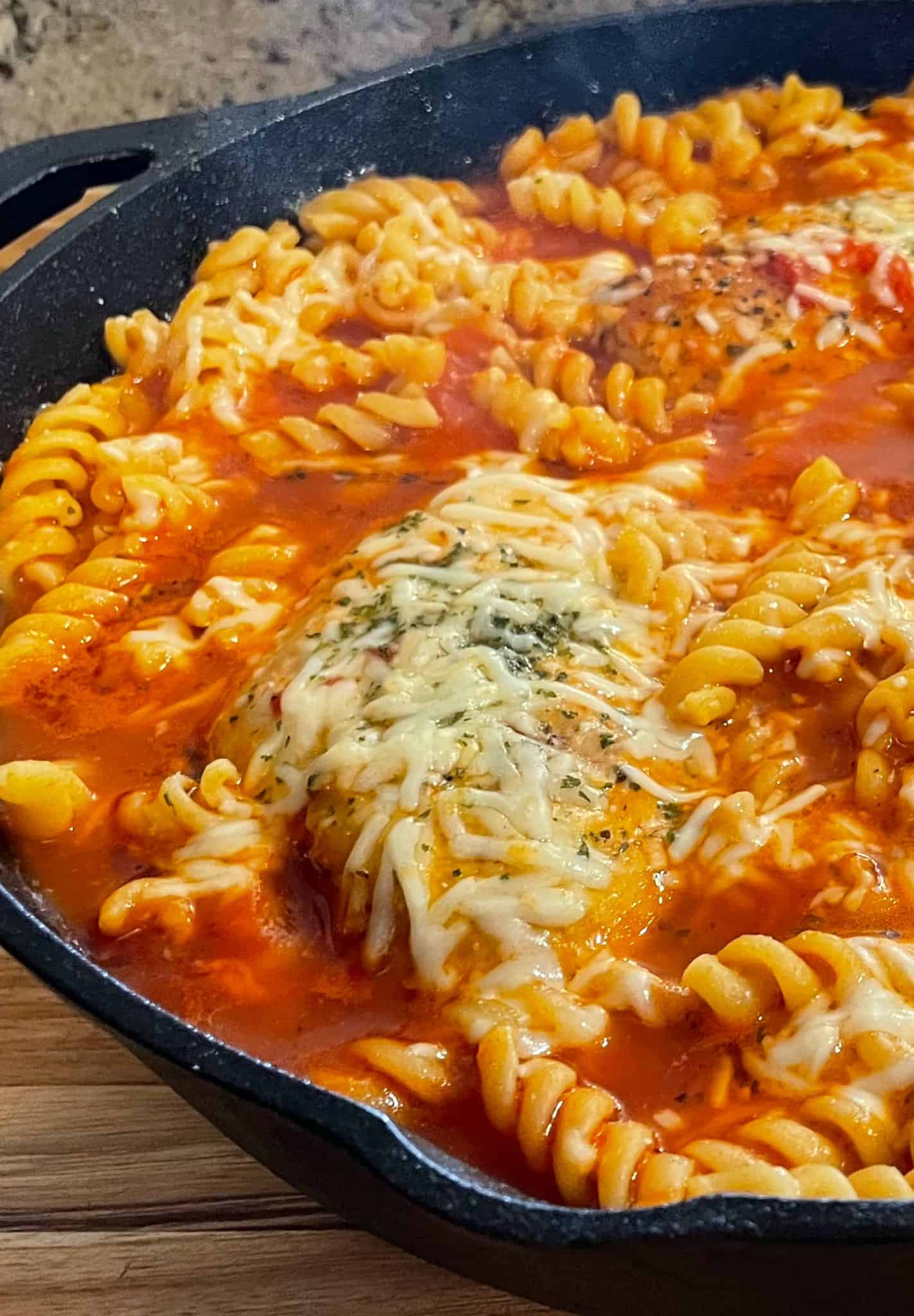 Fusilli pasta and Parmesan cheese added to the skillet with tomato chicken