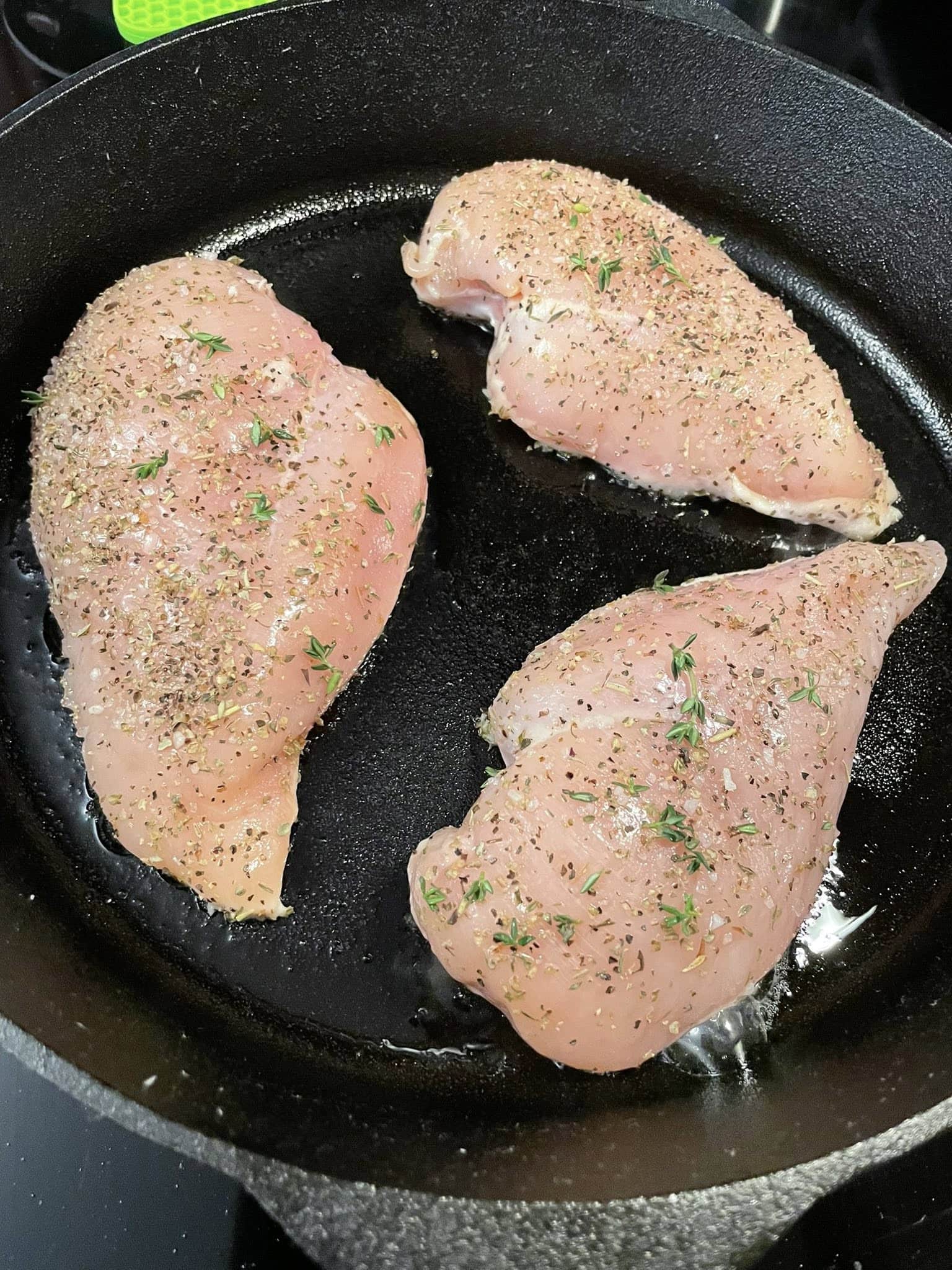 Raw seasoned chicken breasts with thyme searing in a black cast iron skillet