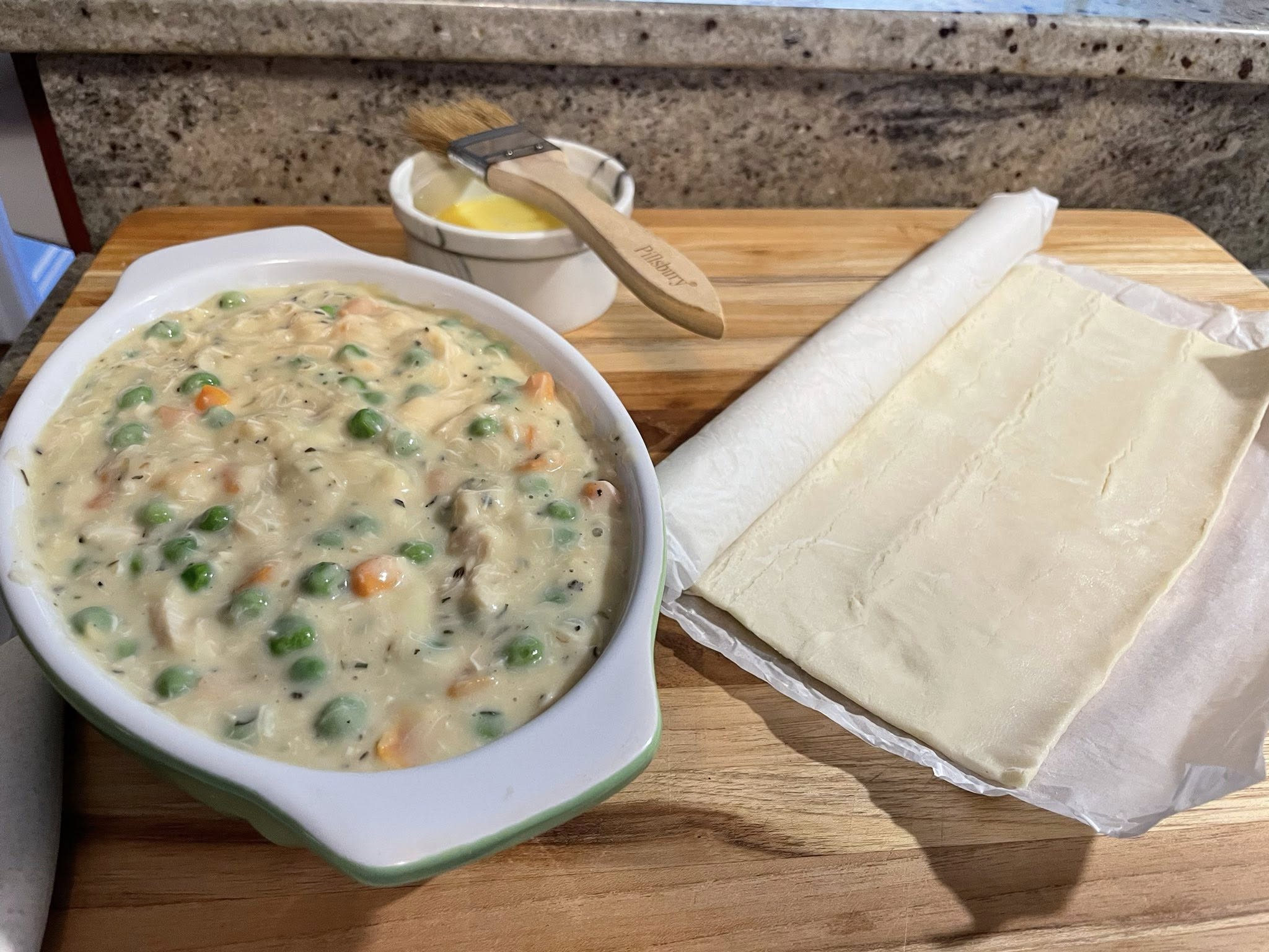  Chicken pot pie filling in baking dish with thawed puff pastry sheet ready to top