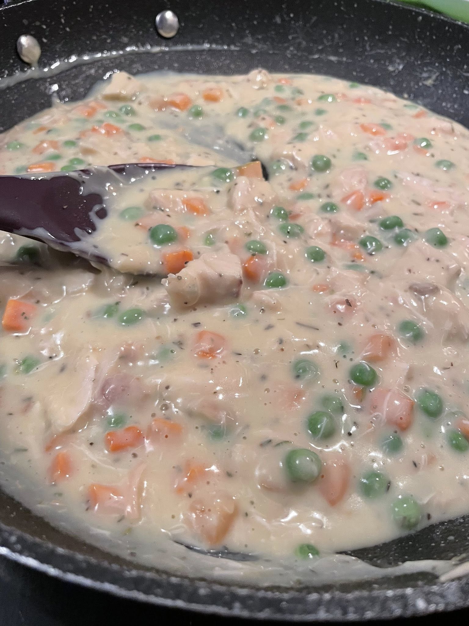 Cooking creamy filling for home down chicken pot pie with puff pastry in skillet with peas, carrots, and diced chicken